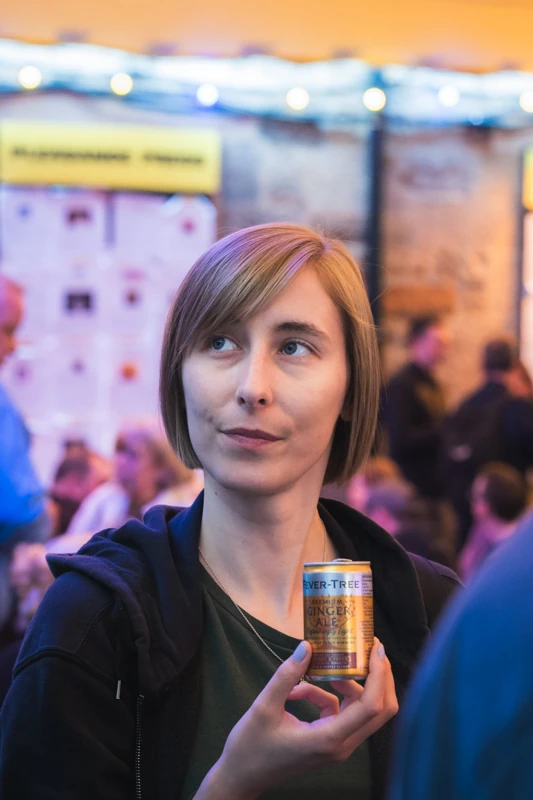 A girl looking upwards and holding a drink against a colourful background.